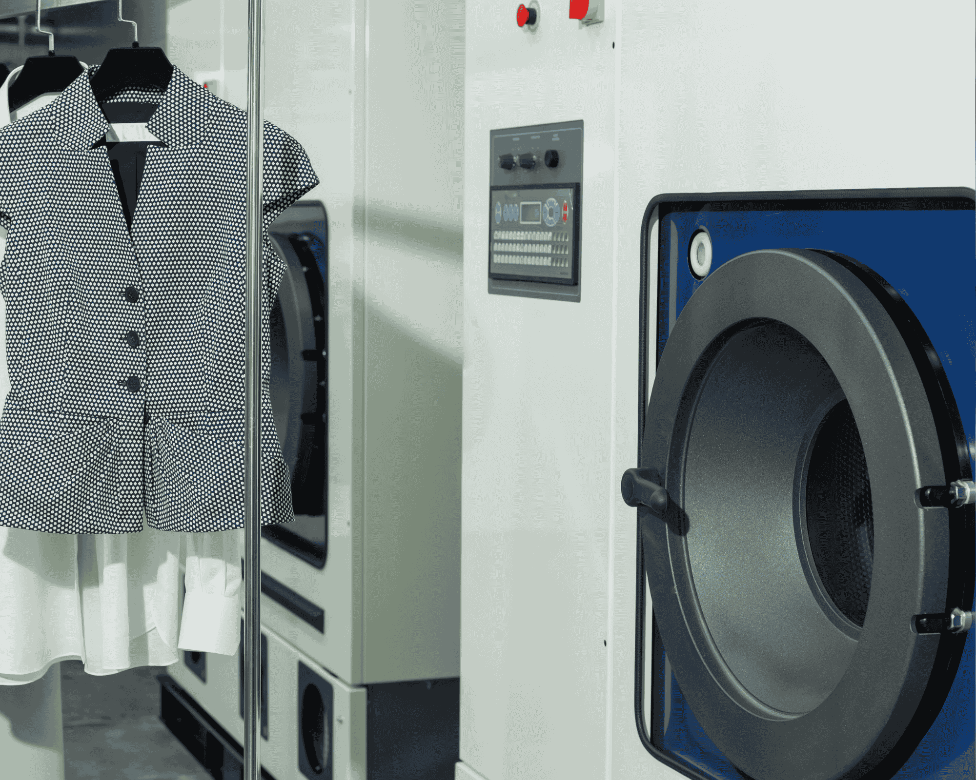 Dry cleaned blouse hanging beside a commercial dry cleaning machine in a professional laundry facility.