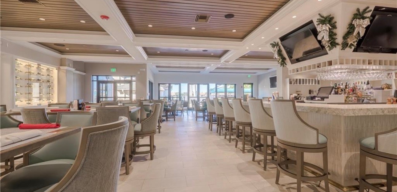 The image depicts the elegant exterior of the Legends Golf and Country Club clubhouse, featuring a beautiful pool area and outdoor dining spaces surrounded by meticulously landscaped grounds. This picturesque setting offers a glimpse of the luxurious amenities available at this premier golf and country club in Central Florida.