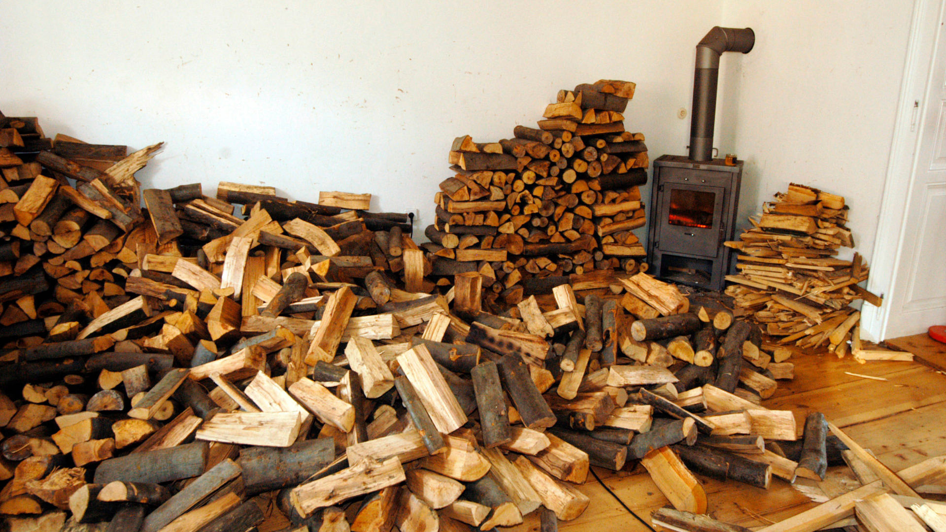 Une pièce remplie de bois de chauffage, avec un poêle à bois et un feu dans la cheminée. 