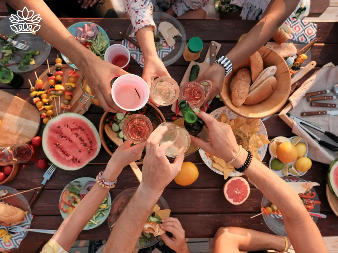 Friends toasting with drinks over a picnic table filled with colourful fruits, salads, and bread. Fabulous Flowers and Gifts - Picnic Gift Baskets Collection.