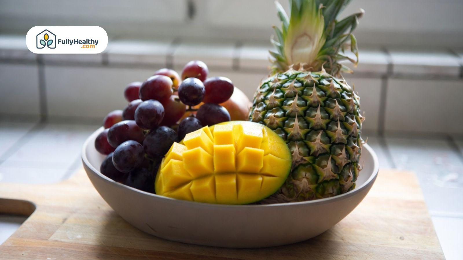 Bowl of fresh fruits including pineapple, grapes, and mango on a counter.