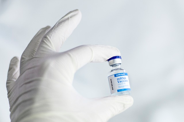 An image of a white gloved hand holding an mRNA vaccine vial. 