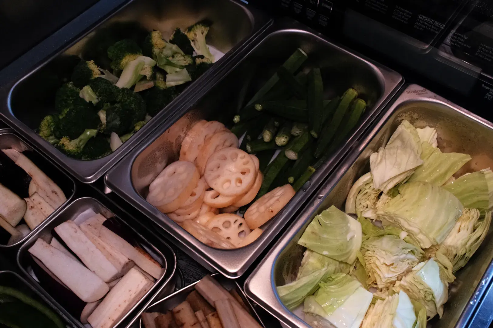 A variety of fresh vegetables in containers, including broccoli, lotus root, okra, and cabbage.