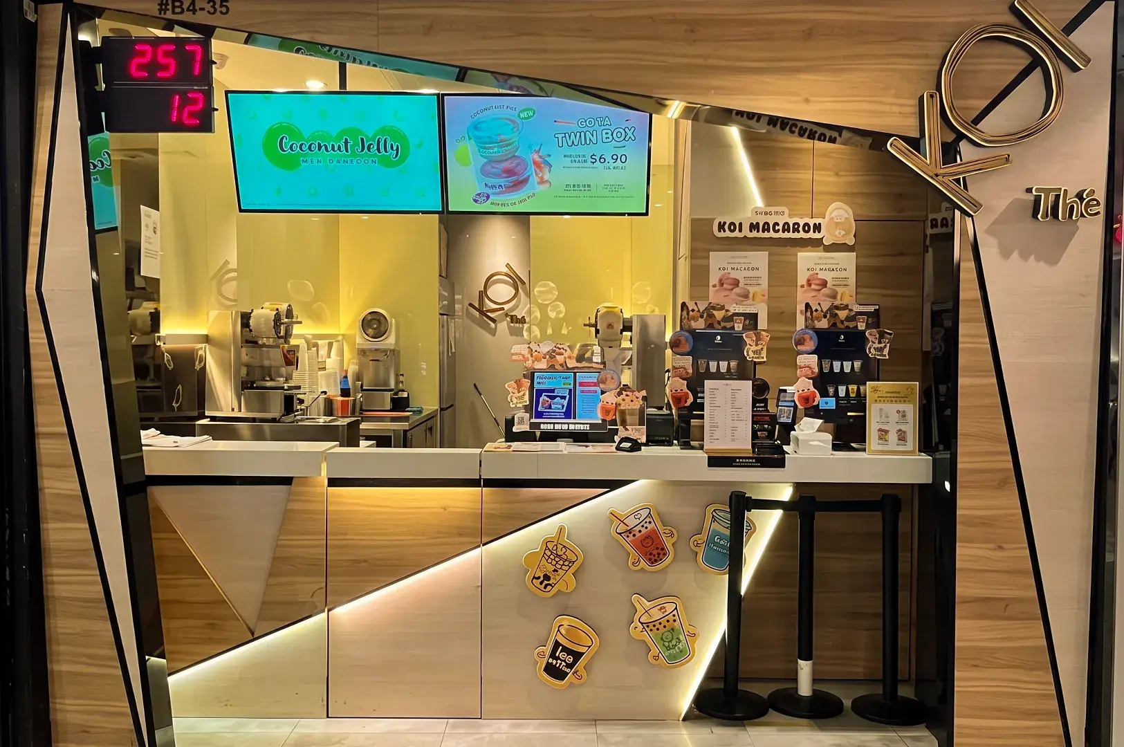 Storefront of a KOI Thé shop featuring a wooden service counter decorated with playful bubble tea illustrations and overhead digital menus.