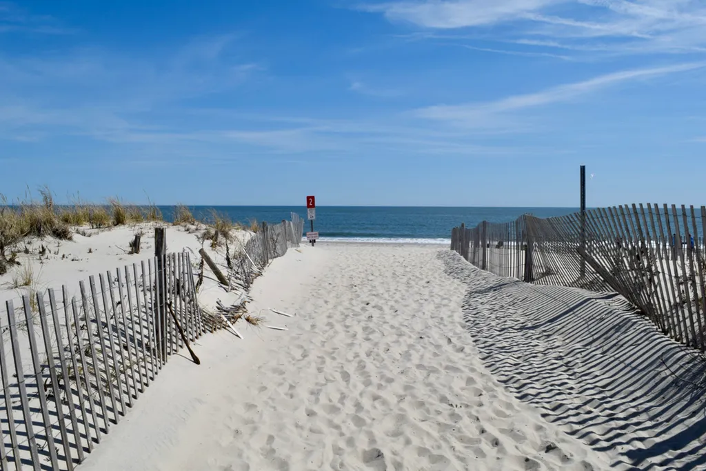 Sandy beach entrance at Cape May near Cape Roc Rentals, with dune fencing leading directly to the ocean shoreline.
