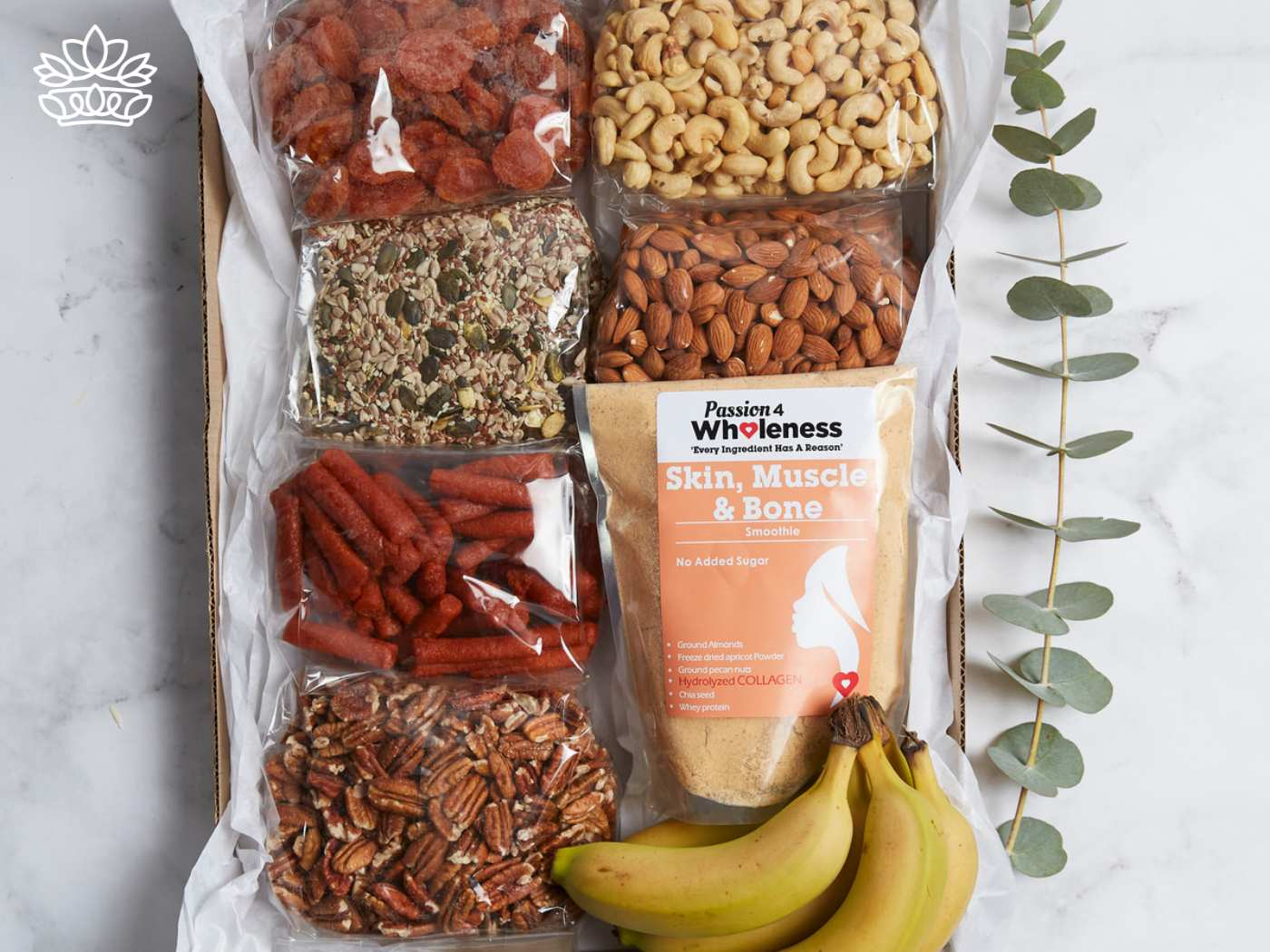 Assorted healthy snack gift box featuring dried strawberries, mixed seeds, seasoned baby carrots, pecans, cashews, and almonds, alongside a 'Passion 4 Wholeness' smoothie mix for skin, muscle, and bone health, adorned with a sprig of eucalyptus. Thoughtfully curated by Fabulous Flowers and Gifts, ideal for guest house and hotel deliveries with a personal touch.