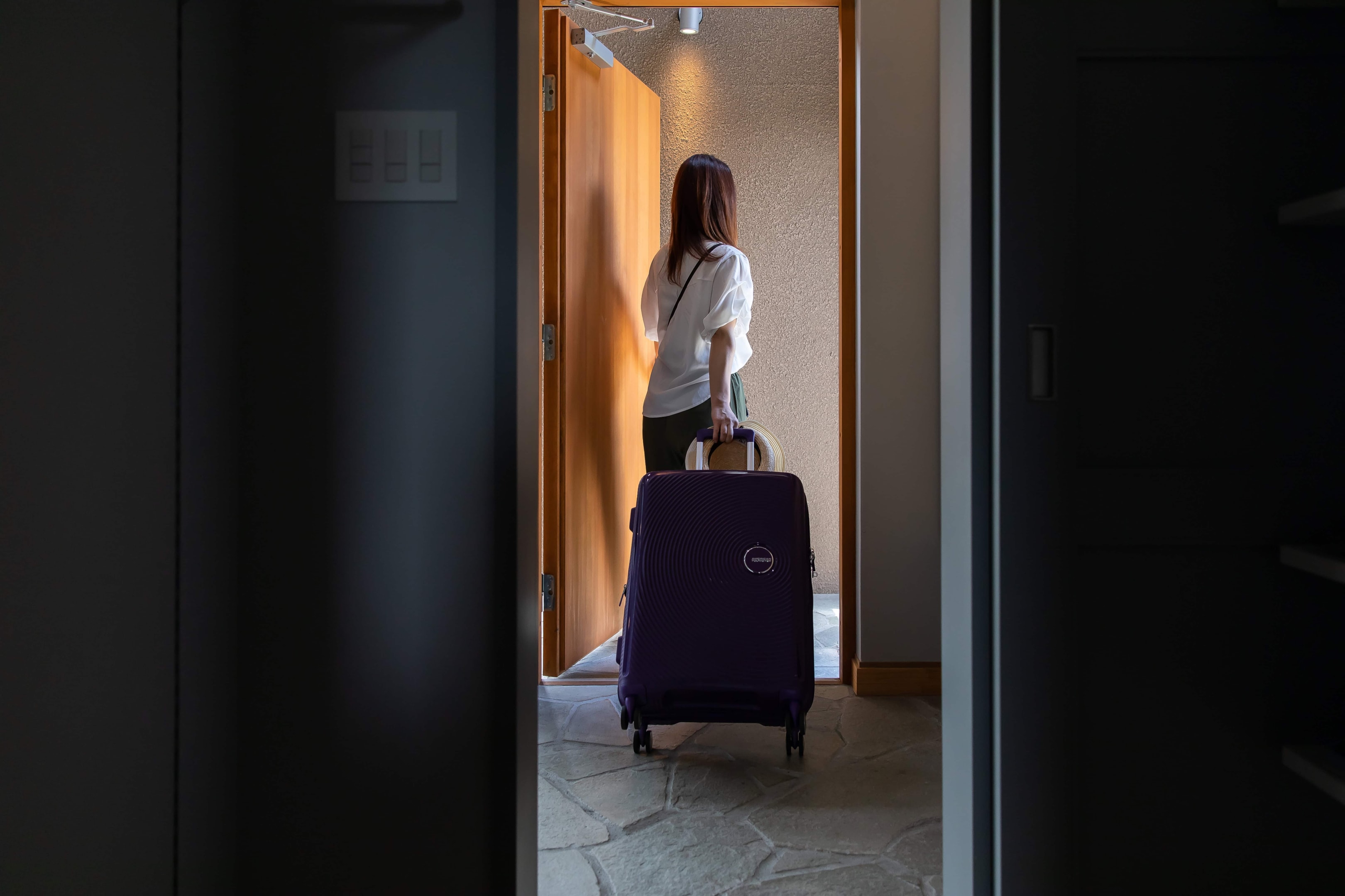 A woman walking out of the door with her luggage.