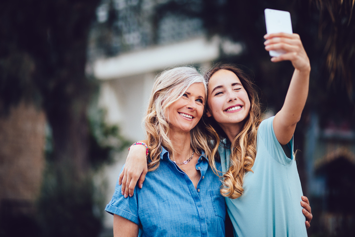 Cheerful young mom and daughter, both in blue shirts, snapping a selfie.