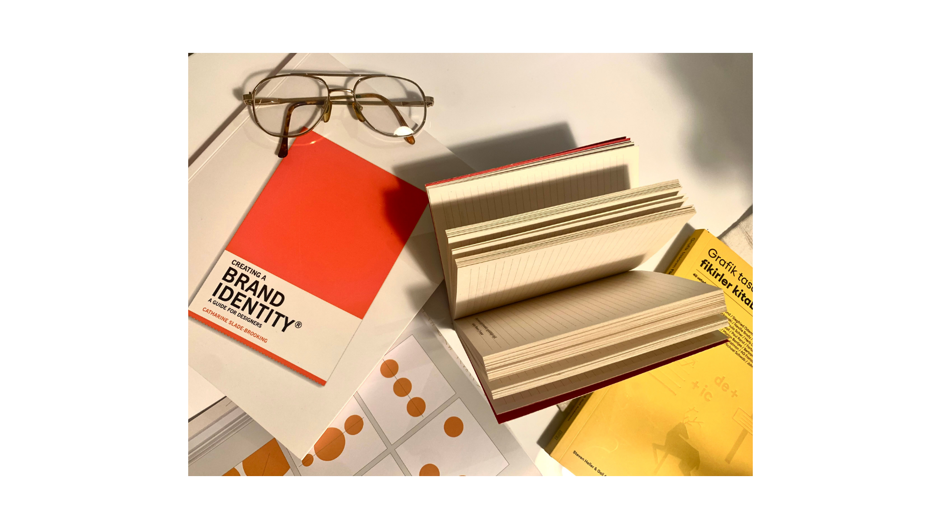 Red notebook saying "brand identity" with glasses and another open notebook next to it. 