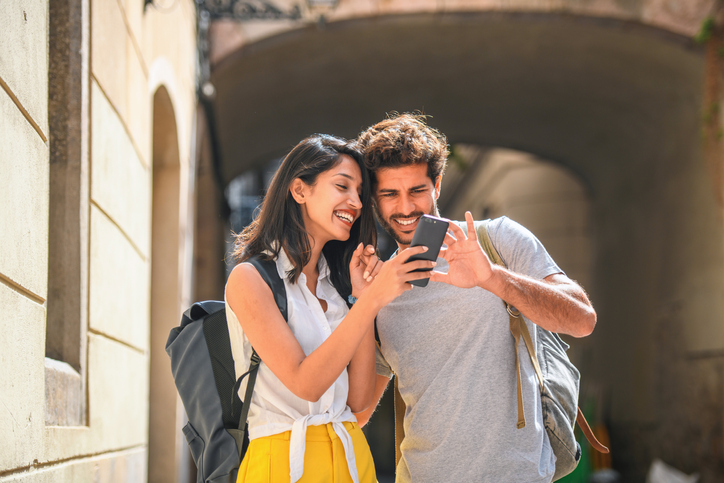 Young couple on vacation smiling and looking at a cell phone.