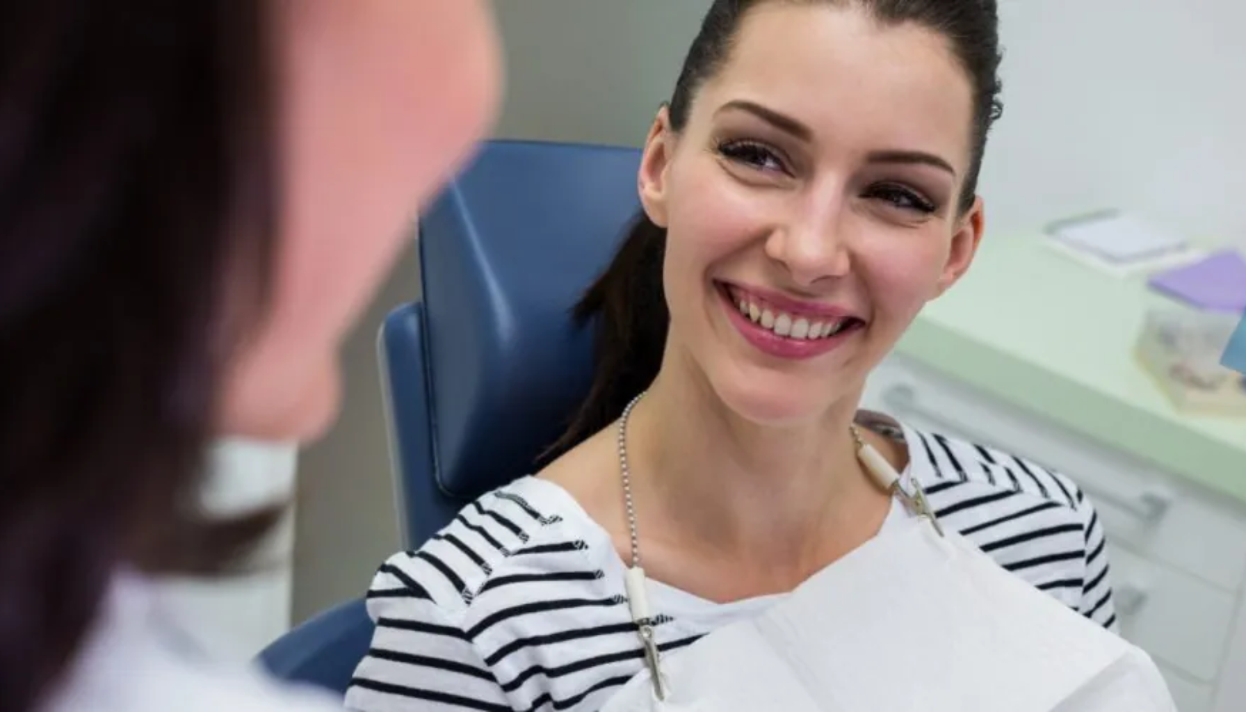 Glad kvinne i tannlegekontor smiler under konsultasjon med røntgen i bakgrunnen.