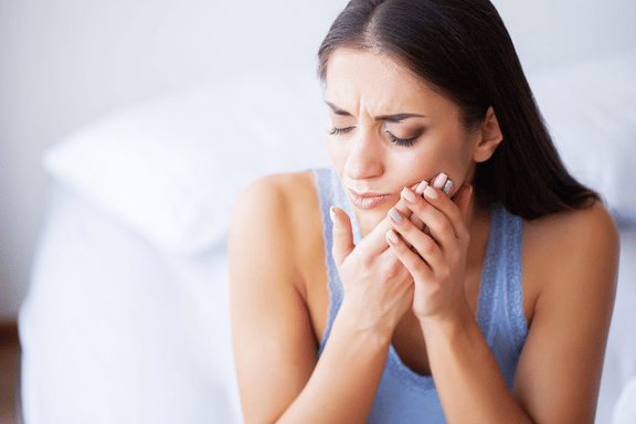 woman holding face wondering how to stop teeth from bleeding after extraction