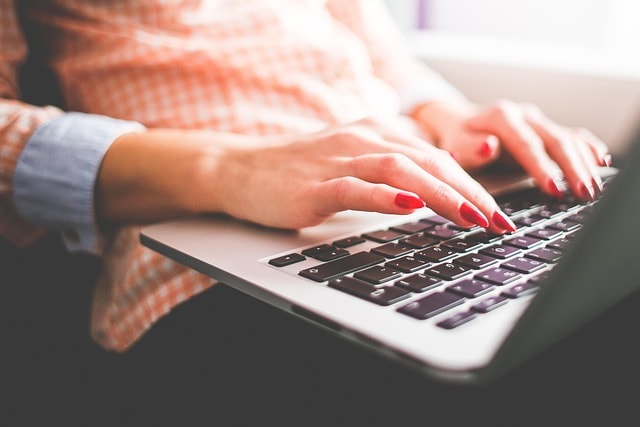 A woman with red nails typing on a laptop representing editing.