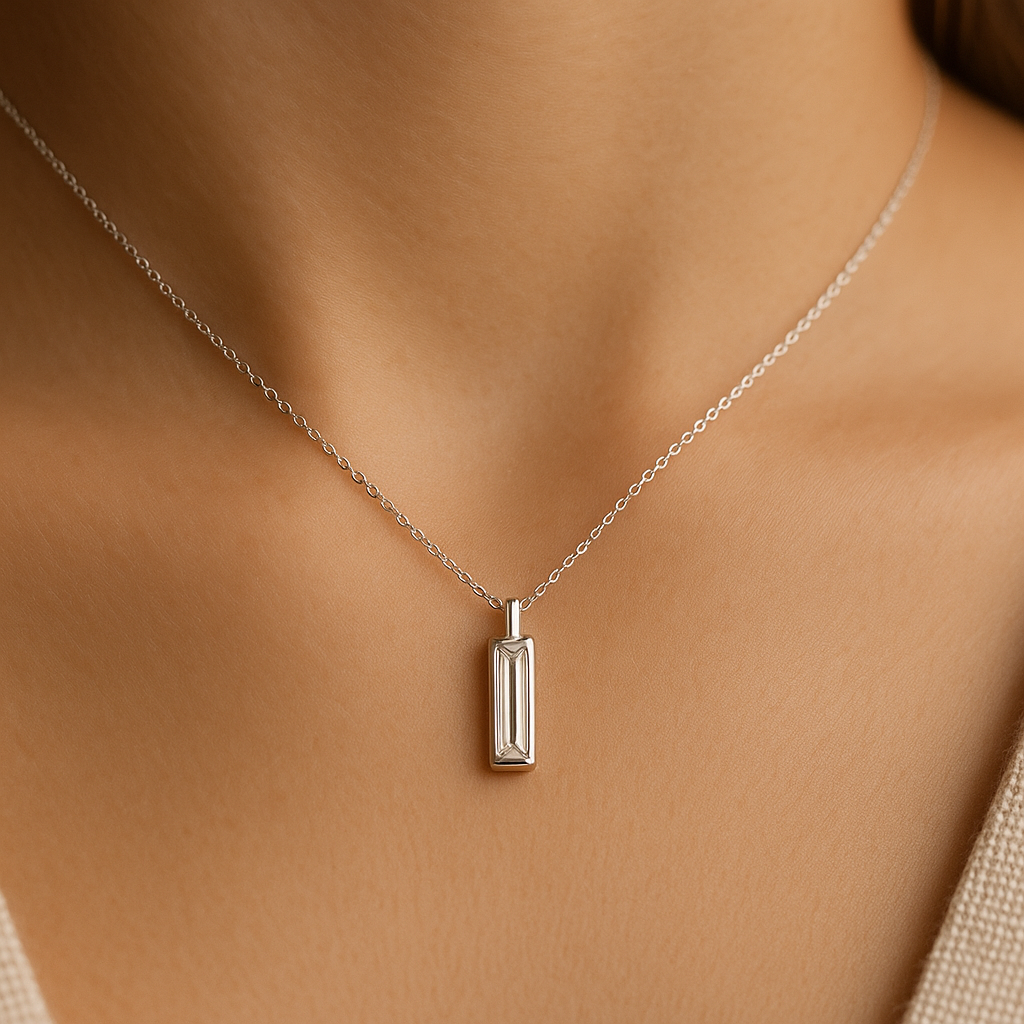 Minimalistinis pakabukas su vertikaliai įstatytu baguette formos deimantu baltame aukse ant moters kaklo.