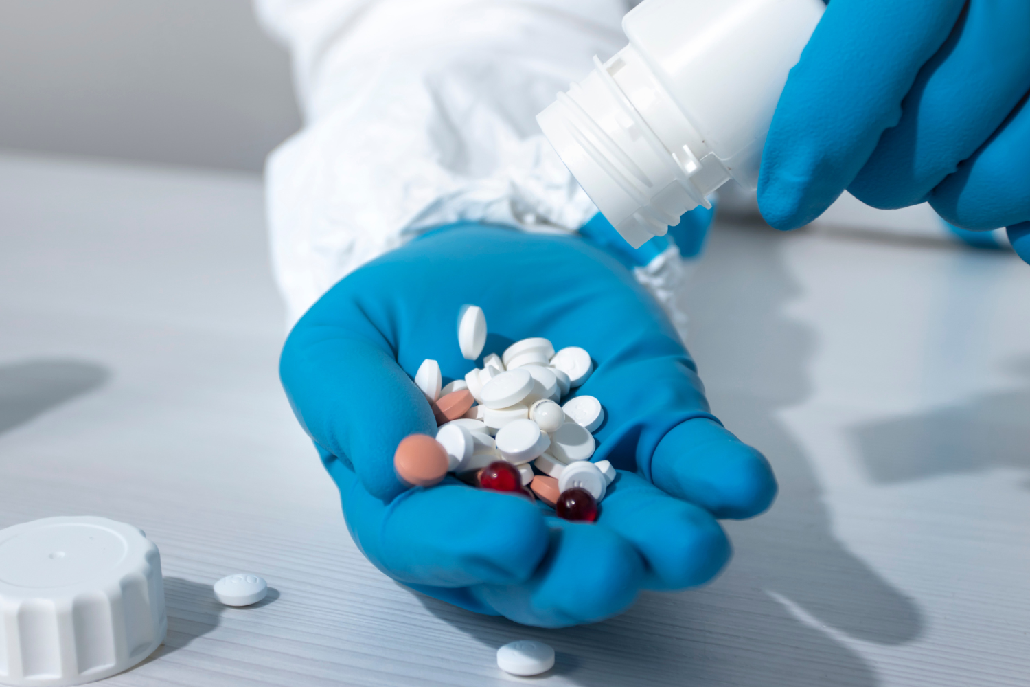 A person pouring tablets on hands while wearing gloves.