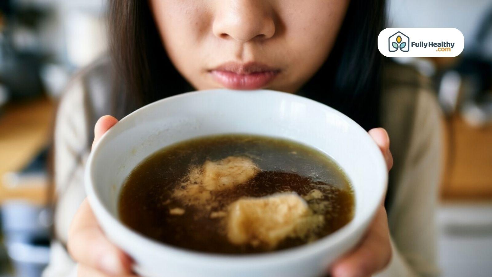 Person smelling a bowl of broth to check freshness and quality.