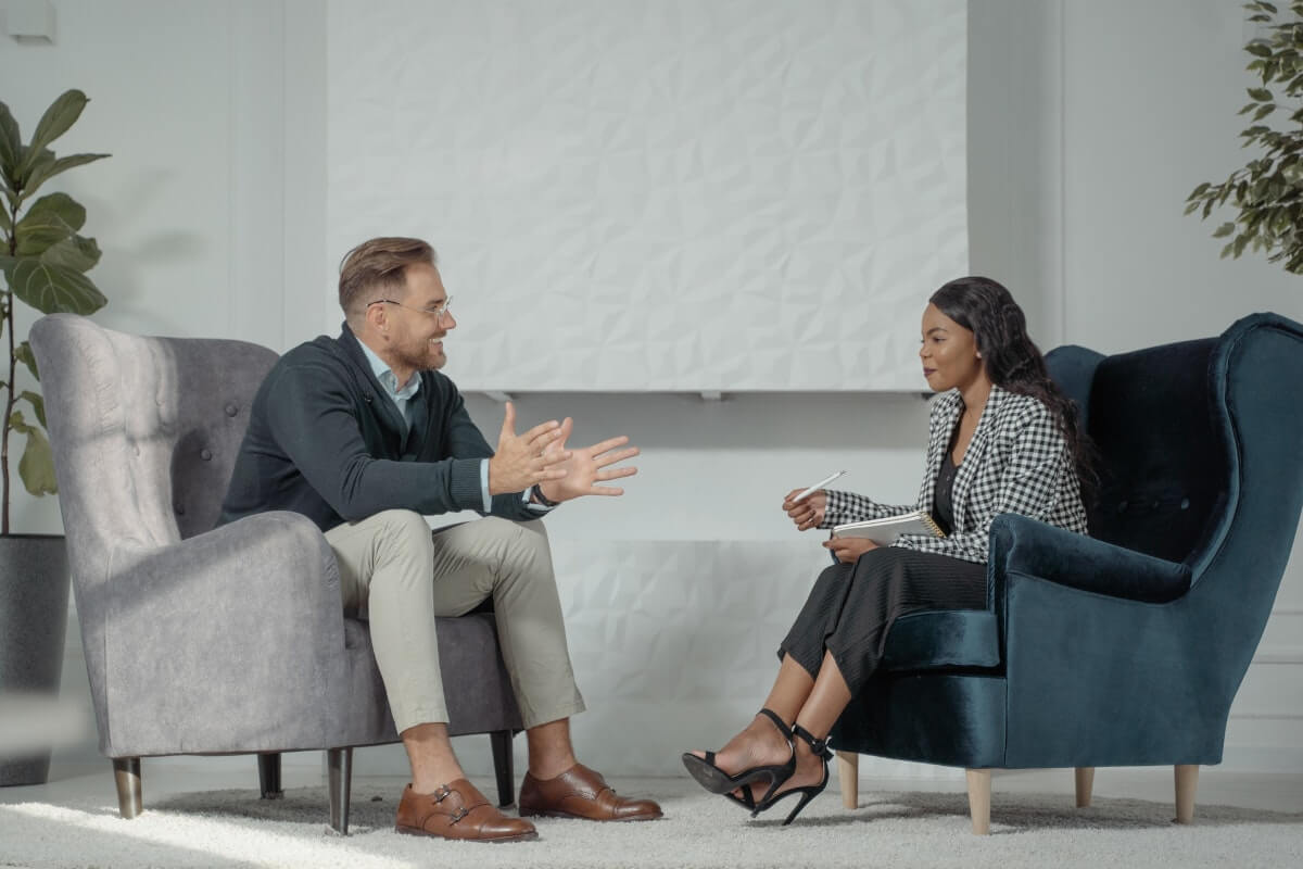 a business owner and a departing employee sitting in armchairs having an informal exit interview