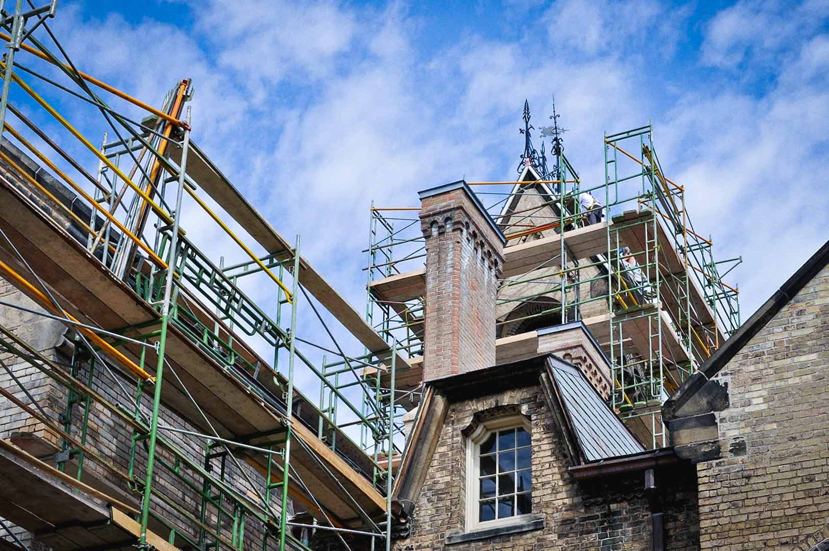 Historic brick building surrounded by scaffolding during restoration under a partly cloudy sky.