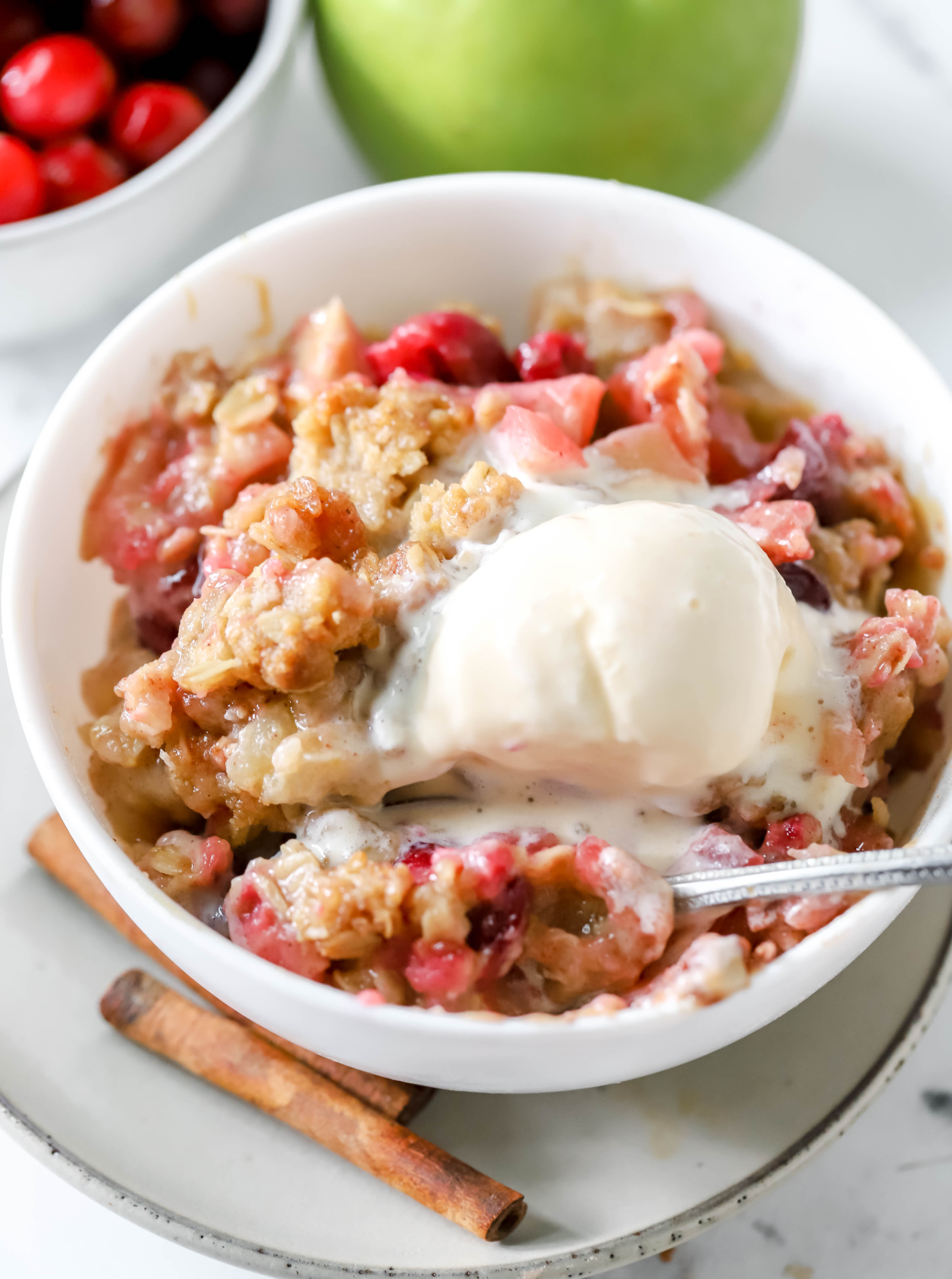 bowl of apple and cranberry crisp topped with vanilla ice cream