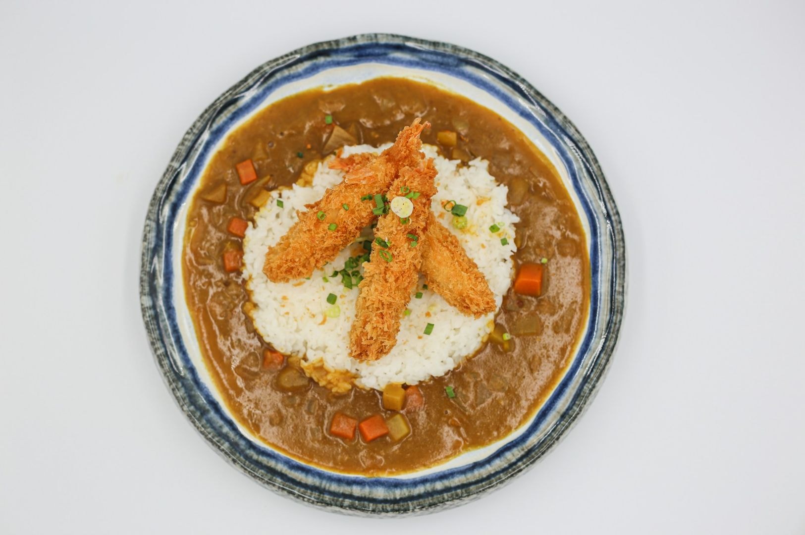 A plate of Japanese curry with breaded shrimp atop a mound of rice, surrounded by rich brown sauce and diced vegetables, garnished with green onions.