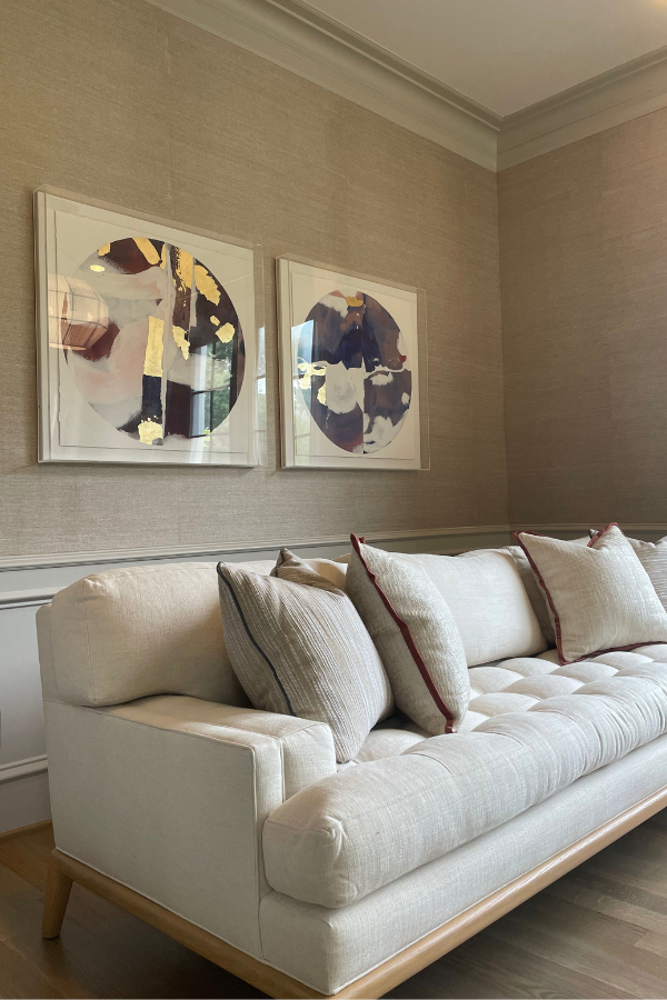 a living room with artwork, a beige sofa, and textured Phillip Jeffries wallpaper