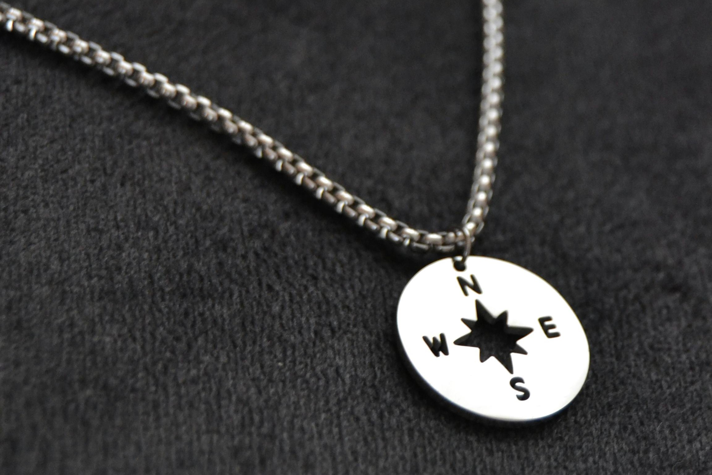 A close-up of a silver-colored stainless steel necklace featuring a compass design.