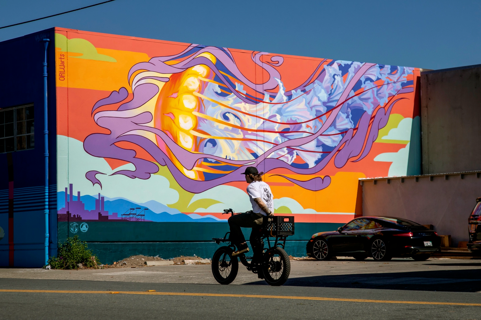 A bicyclist passing in front of a giant colorful mural depicting a jellyfish