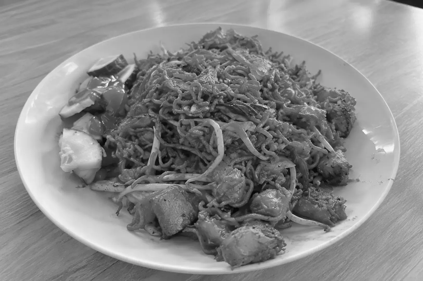 Indian-Muslim mee goreng served on a black plate, with stir-fried noodles, vegetables, tofu, and a savoury sauce.