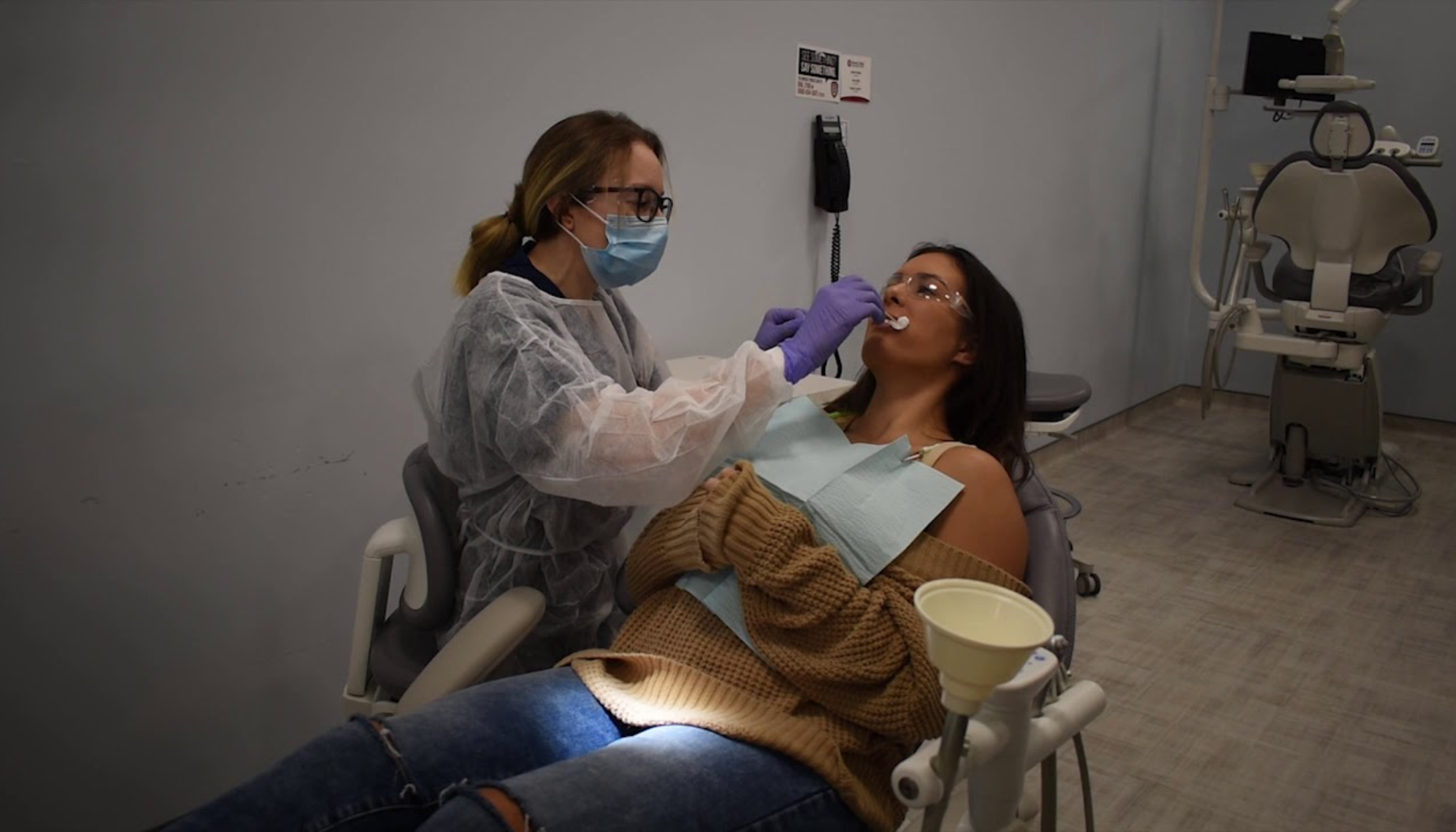 Tannlege med munnbind behandler ung kvinne i tannlegestol under rutinemessig tannundersøkelse i moderne klinikk.