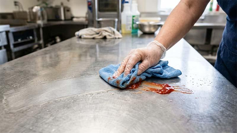 Damp microfiber cloth cleaning a ketchup stain on a stainless steel table