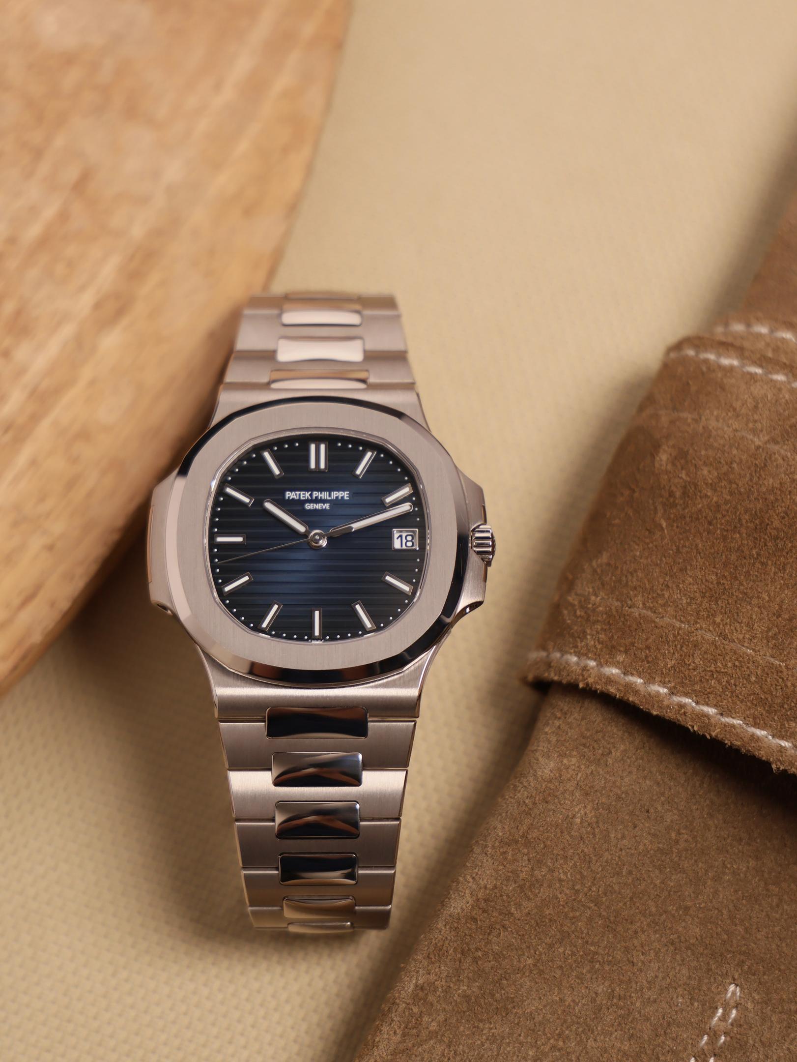 The image depicts a watchmaker's workbench featuring precision tools and an open watch caseback under magnification, showcasing intricate details typical of Patek Philippe designs. The workspace highlights the craftsmanship involved in creating grand complications, reflecting the rich history of watchmaking.