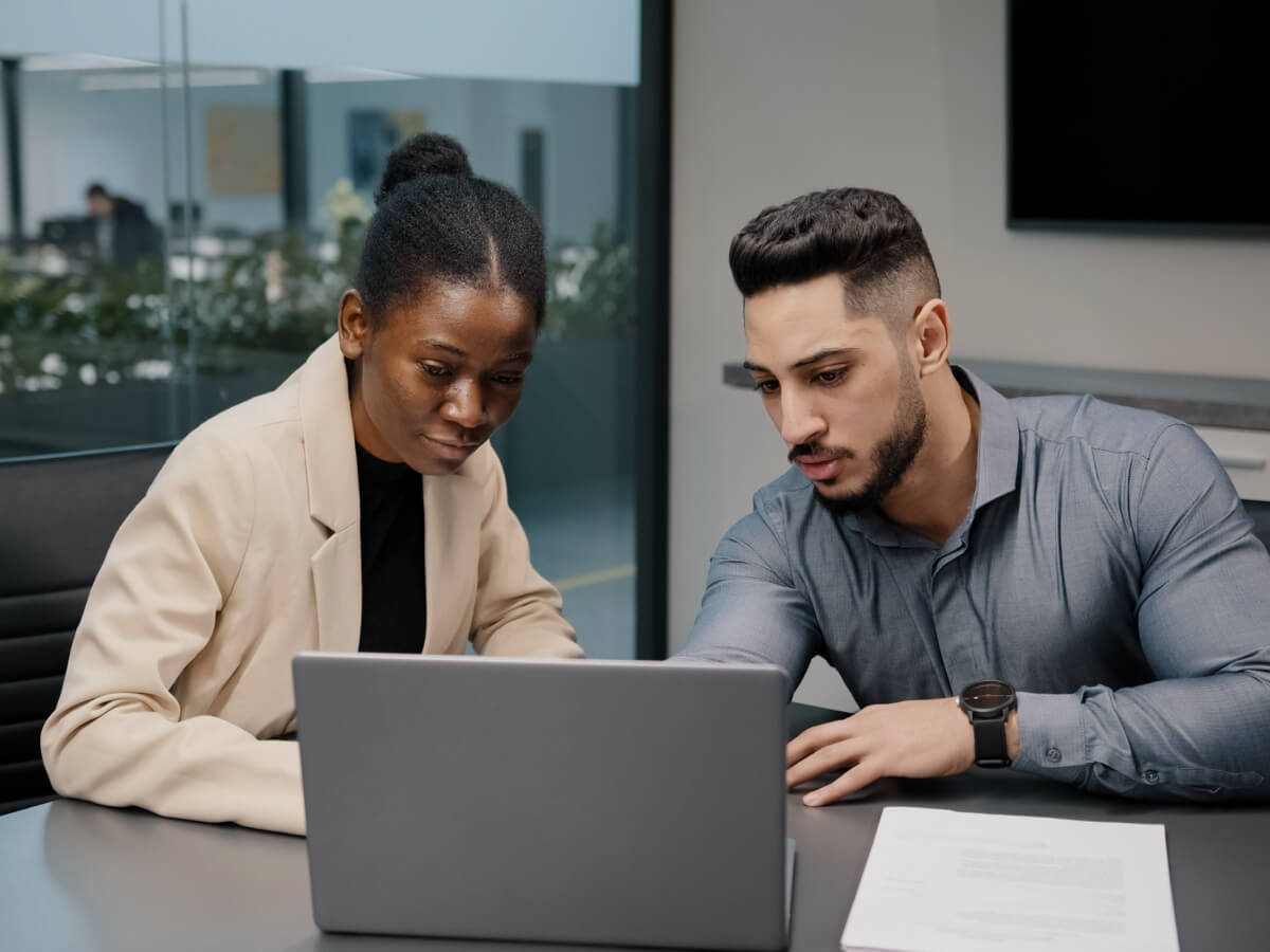 A professional man and woman look at a laptop together in an office