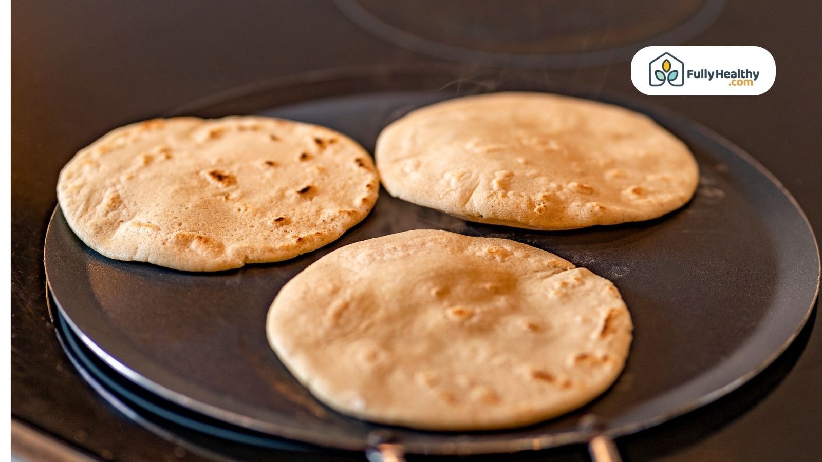 Three fresh tortillas cooking on a flat stovetop skillet