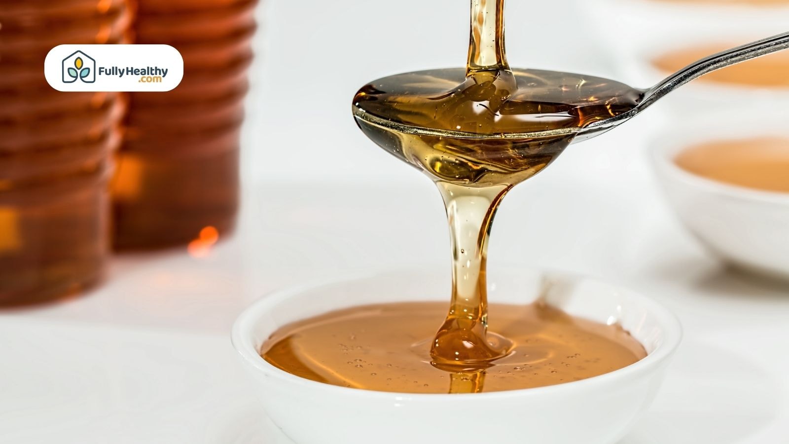 Golden honey dripping from spoon into white bowl