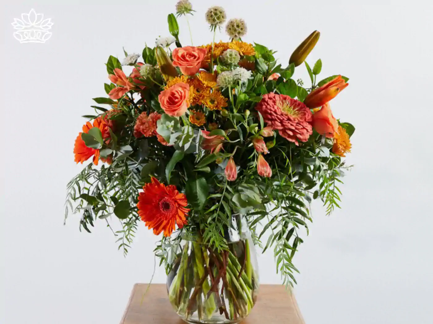 Elegant and beautiful front desk floral display in a glass vase, featuring an assortment of orange blooms, lush greens, and exotic flowers, perfectly arranged to welcome guests.