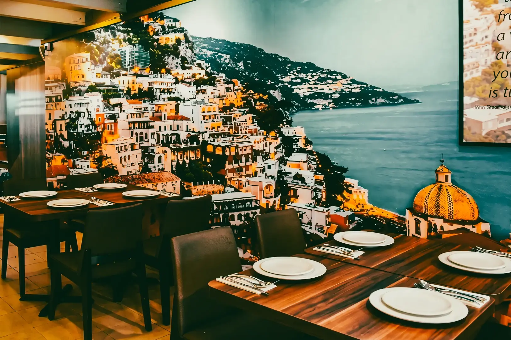 Wide-angle shot of a modern restaurant interior featuring a coastal mural wall, wooden tables with table settings, and a relaxed dining atmosphere inspired by seaside views.