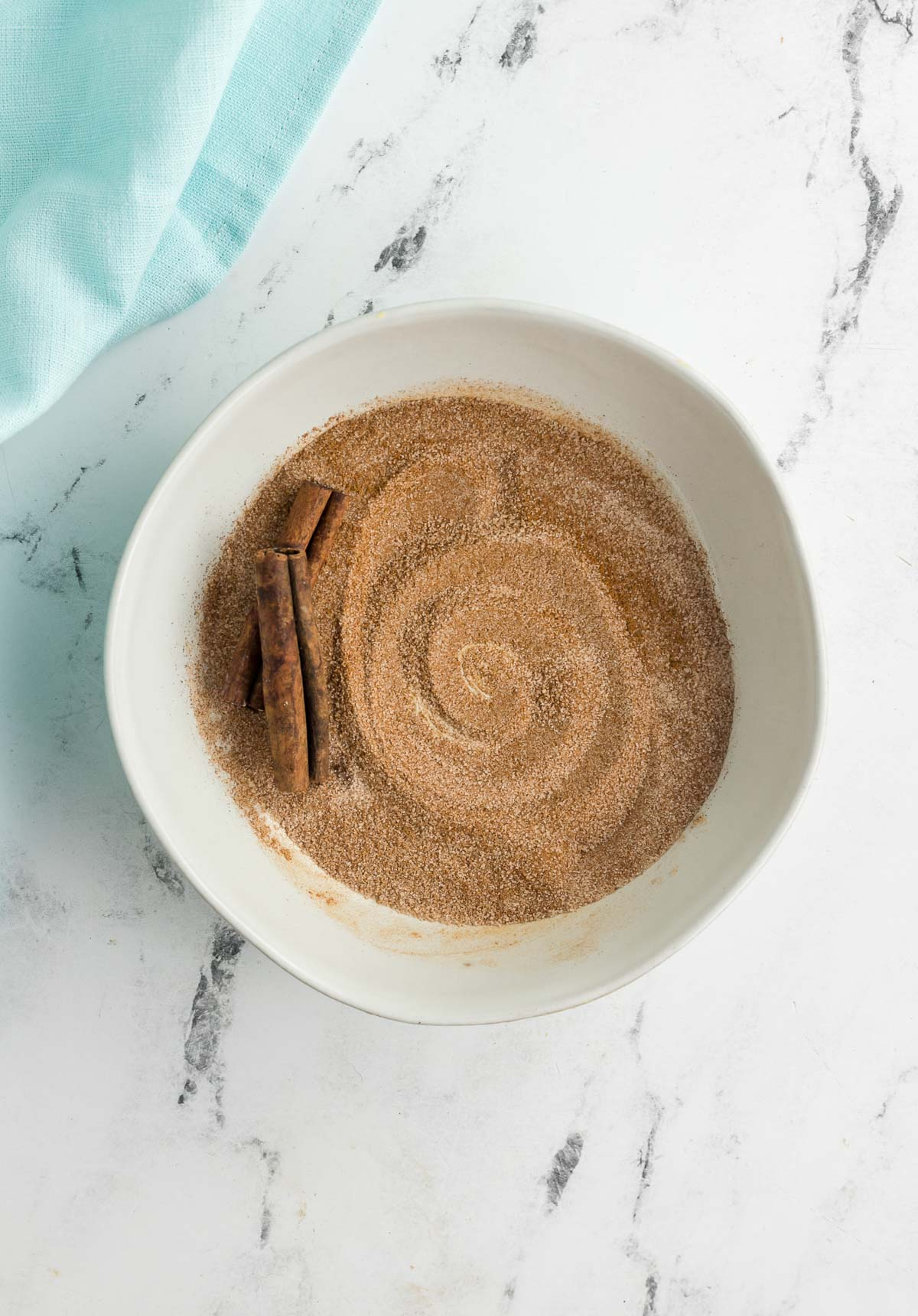 bowl of cinnamon sugar with two cinnamon sticks in it