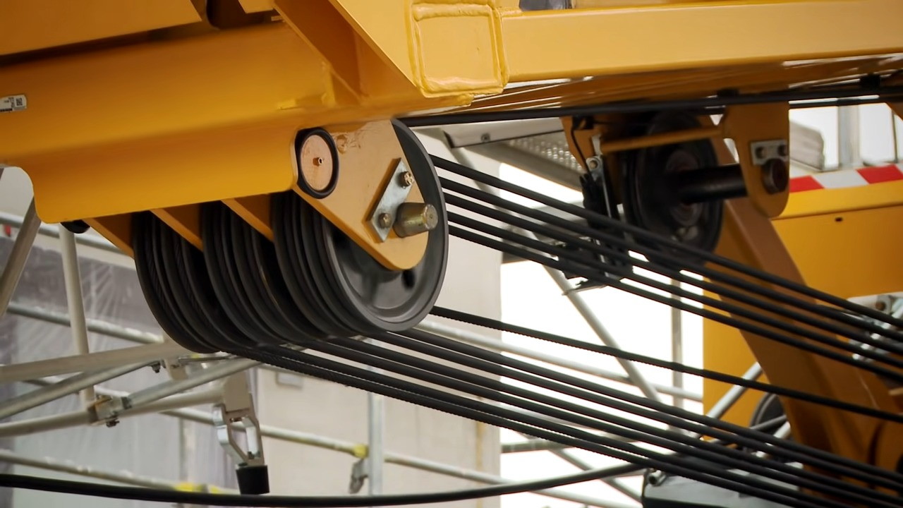 Close-up view of a yellow industrial crane's cable pulley system, featuring organized black cables and mechanical parts showing innovations in design