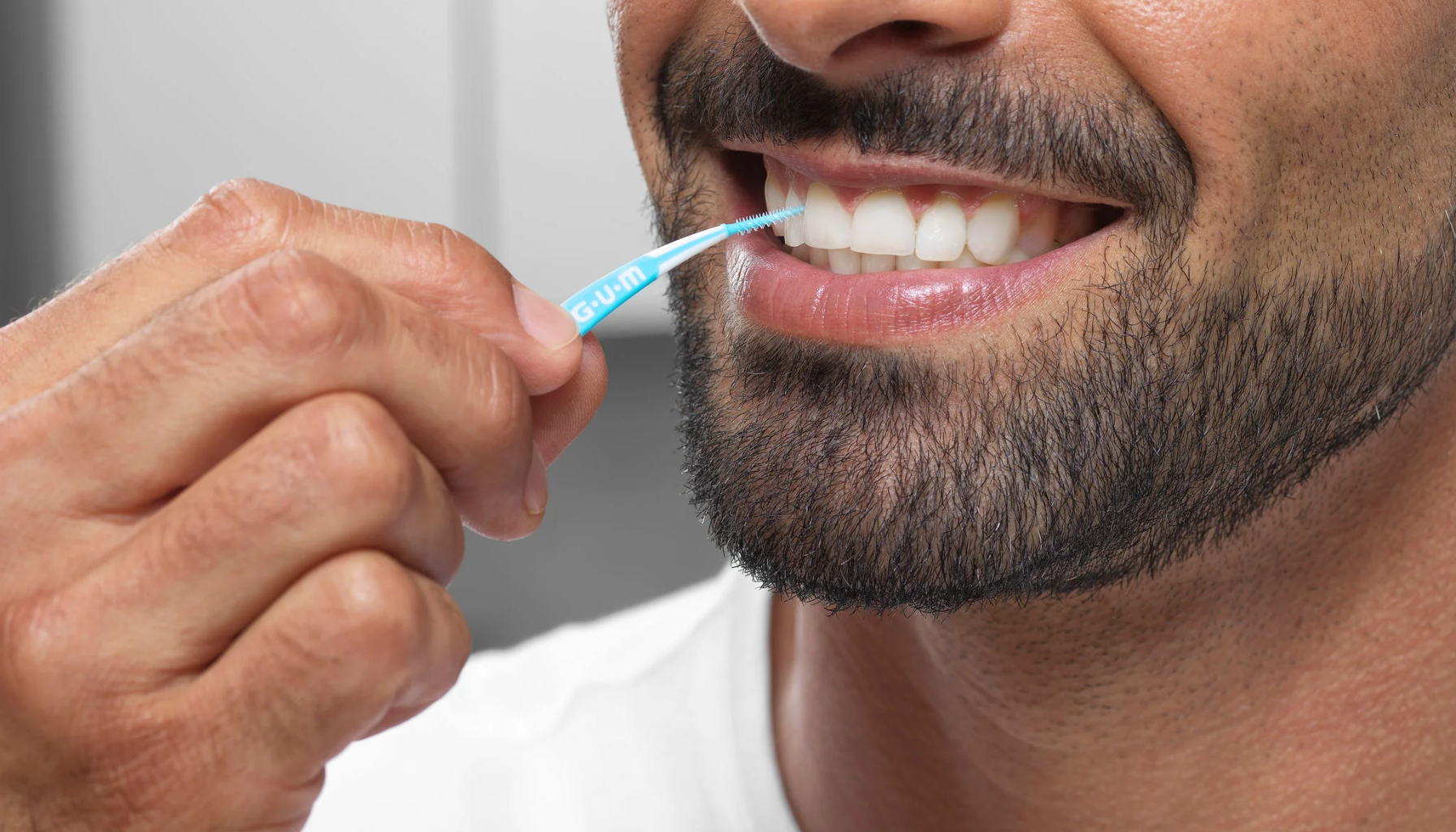 Mellomromsbørste: Det Beste Verktøyet for Renhold Mellom Tennene 11 Nærbilde av mann som bruker interdentalbørste for å rense mellom tennene, med synlig skjegg og smil hjemme.