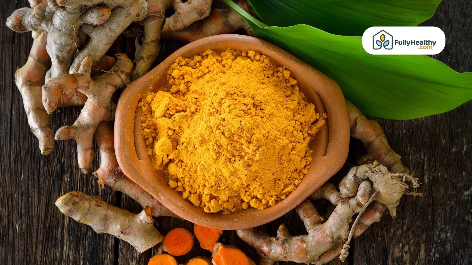 Ground turmeric in a clay bowl surrounded by whole turmeric roots on a rustic wooden surface