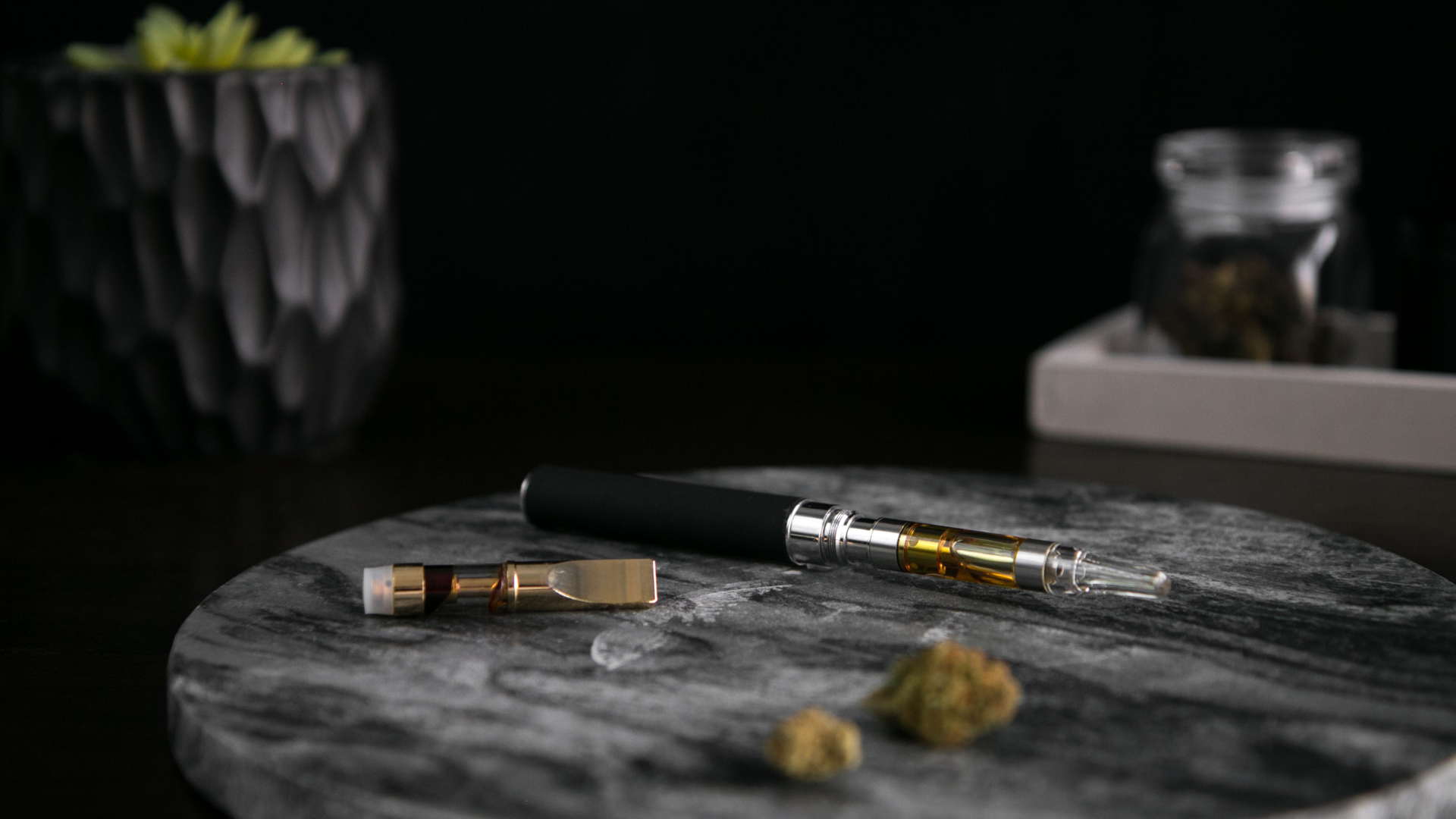 cannabis vape pen laying on a table with a marijuana pod
