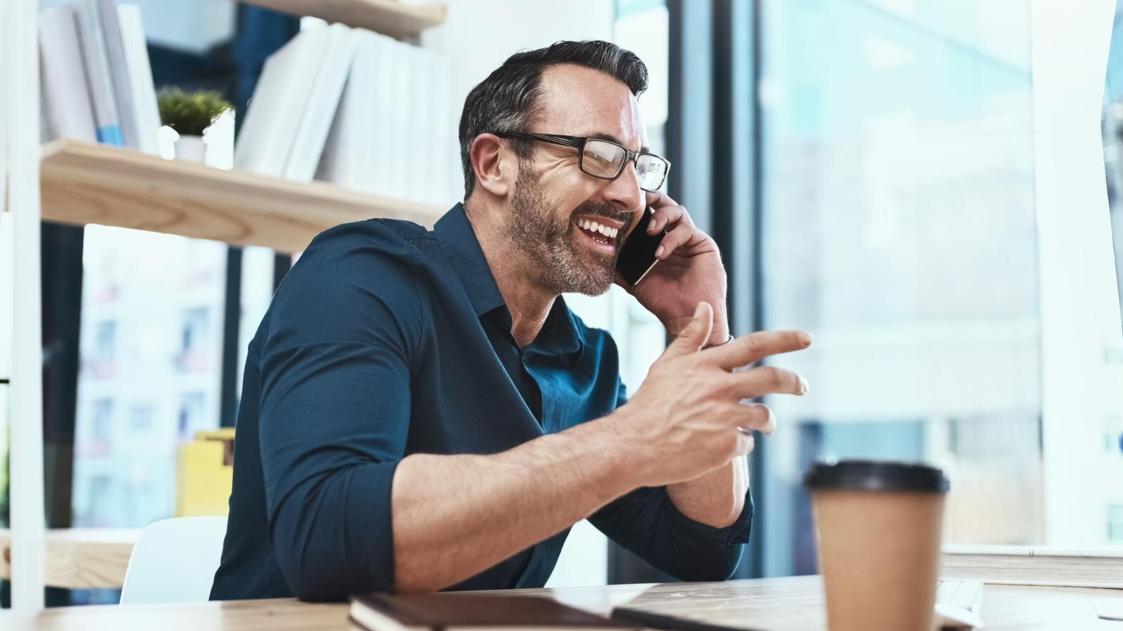 Smiling man on phone in office, happy with his quick setup, easy-to-assign phone numbers and combined voice and video calls via TeamMate.