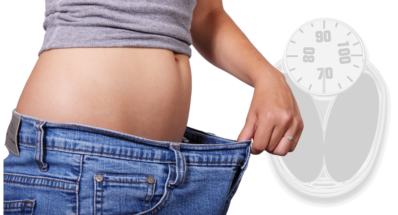 An image of a woman pulling the waistband of her jeans away from her belly to show her weight loss. 