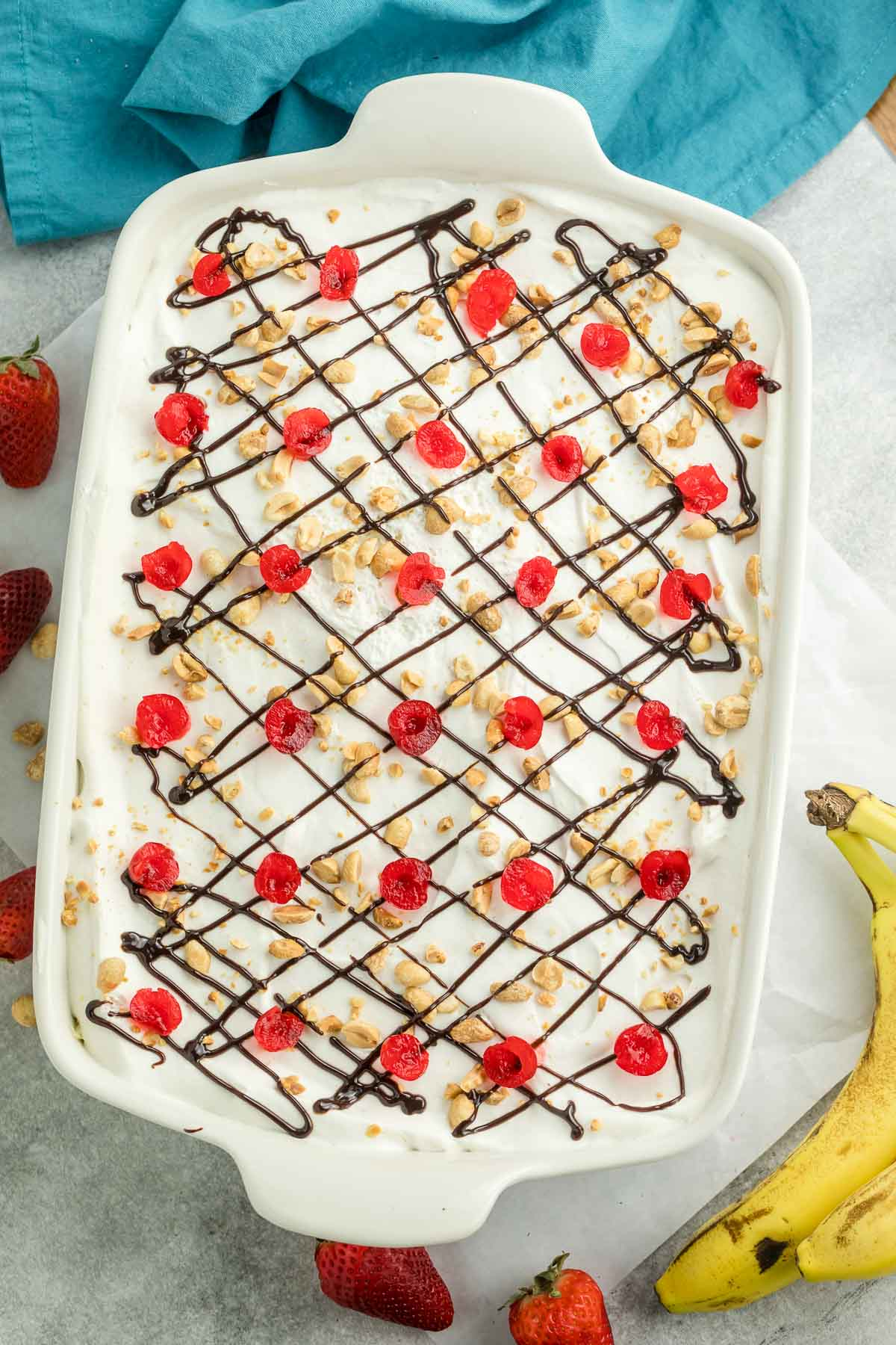 banana split cake topped with hot fudge, maraschino cherries, and peanuts