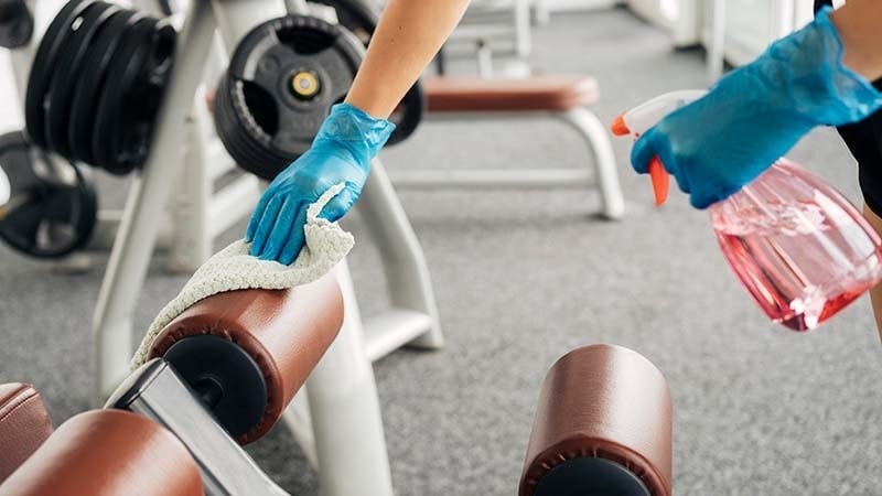 A man disinfects gym equipment