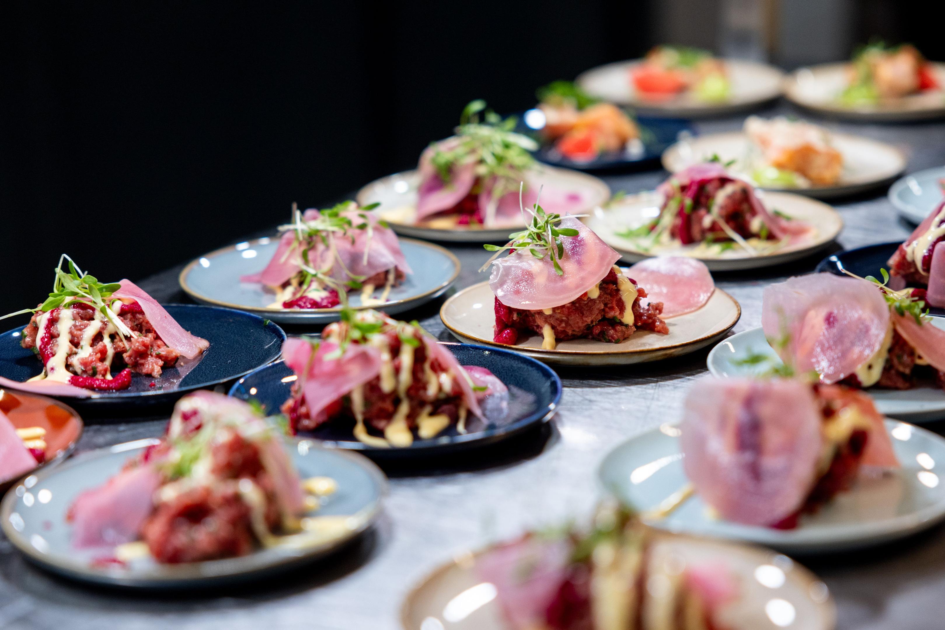 The image depicts a bustling restaurant kitchen pass station during a busy dinner service, filled with tickets and beautifully plated dishes ready for service. The scene highlights the importance of effective kitchen management and food quality as the kitchen team works efficiently to ensure customer satisfaction.