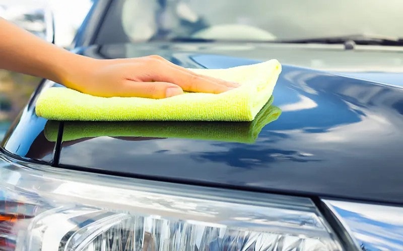 A person cleans the front of a car with a microfiber cloth
