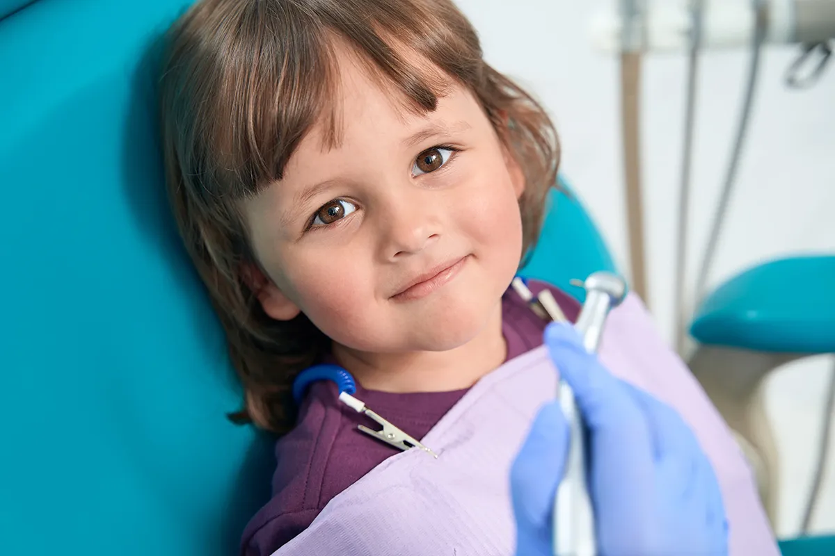 Smiling child patient with dental bib in dental examination chair.