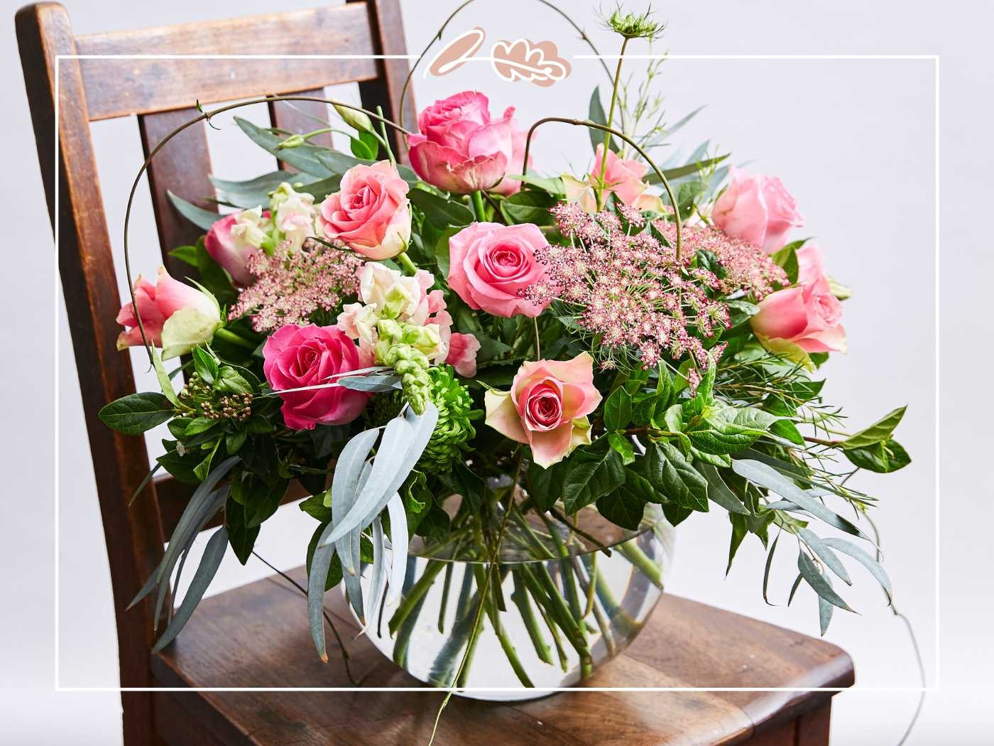 A luxurious arrangement of pink roses and greenery in a glass bowl, placed on a wooden chair - Fabulous Flowers and Gifts