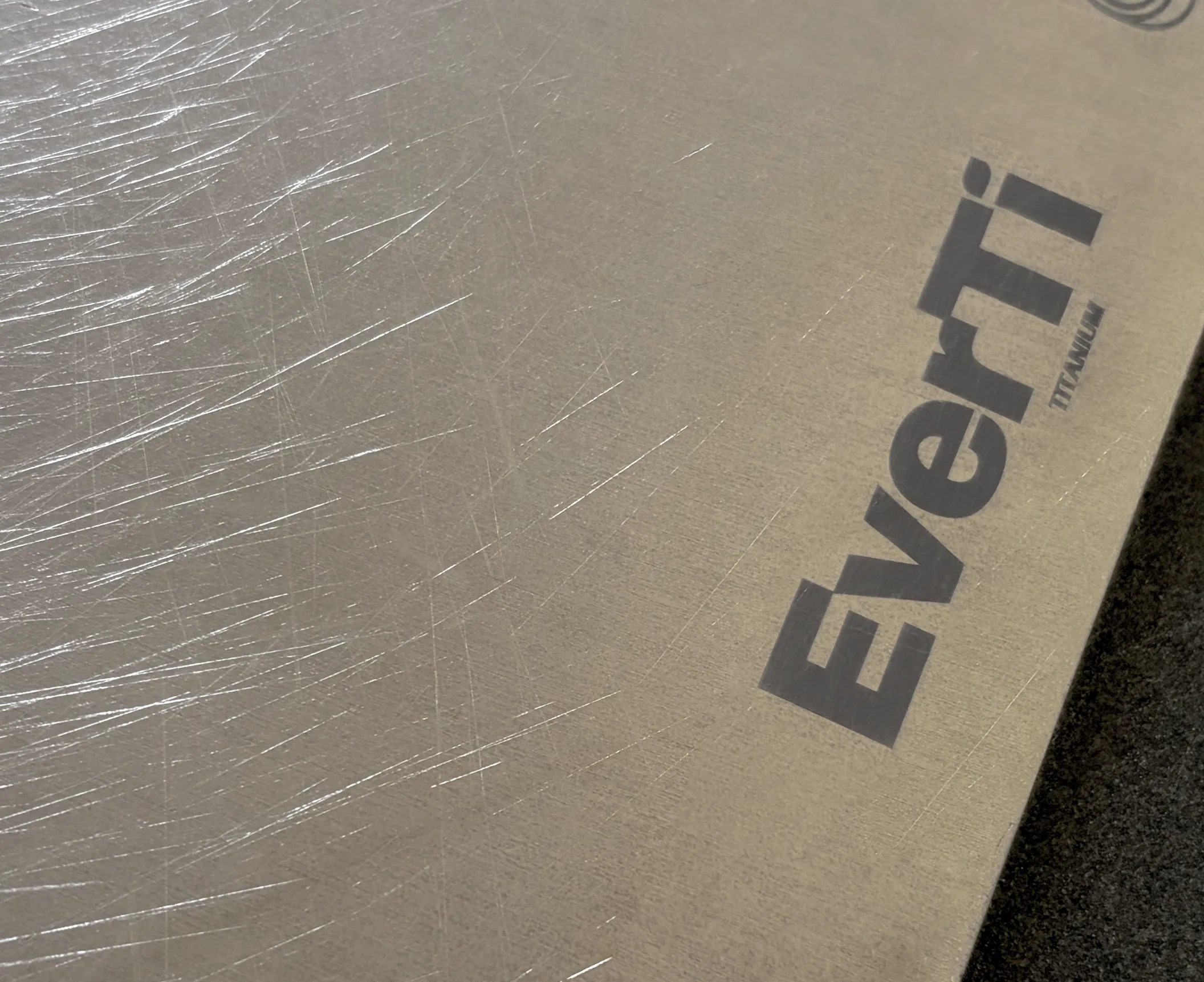 A close-up view of a titanium cutting board surface reveals light scratches and cut marks, showcasing its durability and non-porous material under kitchen lighting. This heavy-duty board is ideal for long-term use, providing a reliable surface for slicing and dicing food.